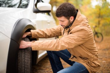 Young bearded man checking car tyre in autumn forest