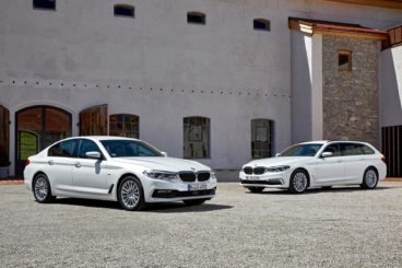two BMW's parked on gravel driveway in front of large house