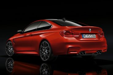 The back of a metallic red bmw m4 coupe isolated on a black background