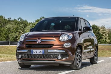 a metallic coloured Fiat 500l parked on a road with green trees in the background