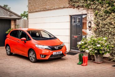 Orange Honda Jazz parked outside a house with a garage and wellington boots by the door