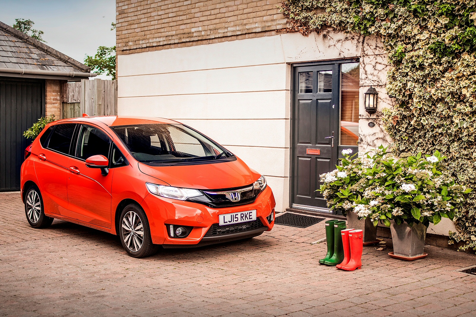 Orange Honda Jazz parked outside a house with a garage and wellington boots by the door