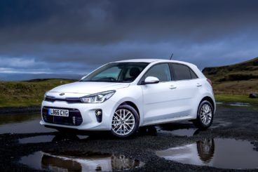 A white kia rio hatchback parked in a puddle in front of some hills