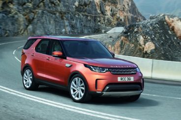 Orange Land Rover Discovery driving around a corner on the road in the mountains