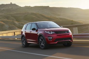 red land rover discovery sport diesel driving on a road at sunset