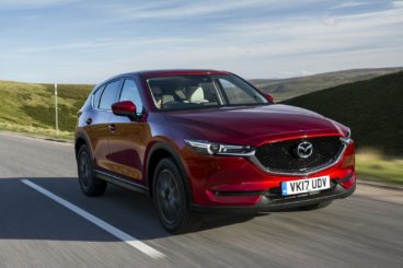 Red Mazda CX-5 driving on a country road with hills in the background