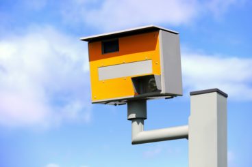 yellow speed camera in front of blue sky with clouds