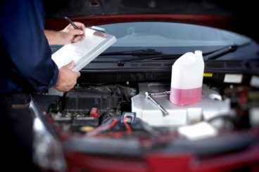 mechanic writing down notes on car with cooler fluid and spanner on top of engine