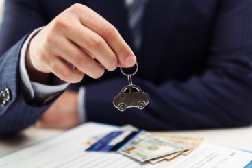 business man in blue suit holding car key ring over car leasing documentation