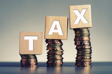 3 wooden blocks standing on stacks on coins spelling out the word tax