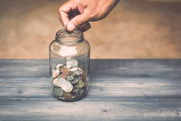 man putting more coins into a savings coin jar