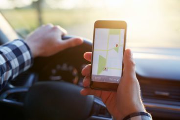 man in checked shirt driving whilst looking at a map on his phone
