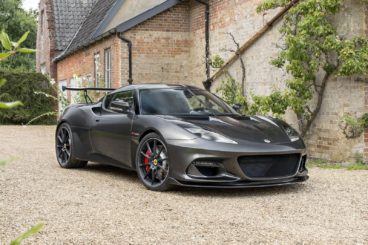 dark grey lotus evora coupe parked on pebble driveway next to country road