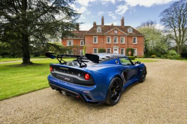 the back of a bright blue lotus exige coupe parked on gravel driveway infront of country house