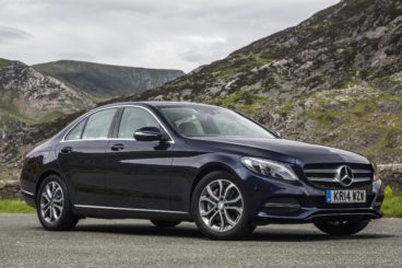 A dark blue mercedes benz c class amg saloon parked on tarmac with mountains in the background