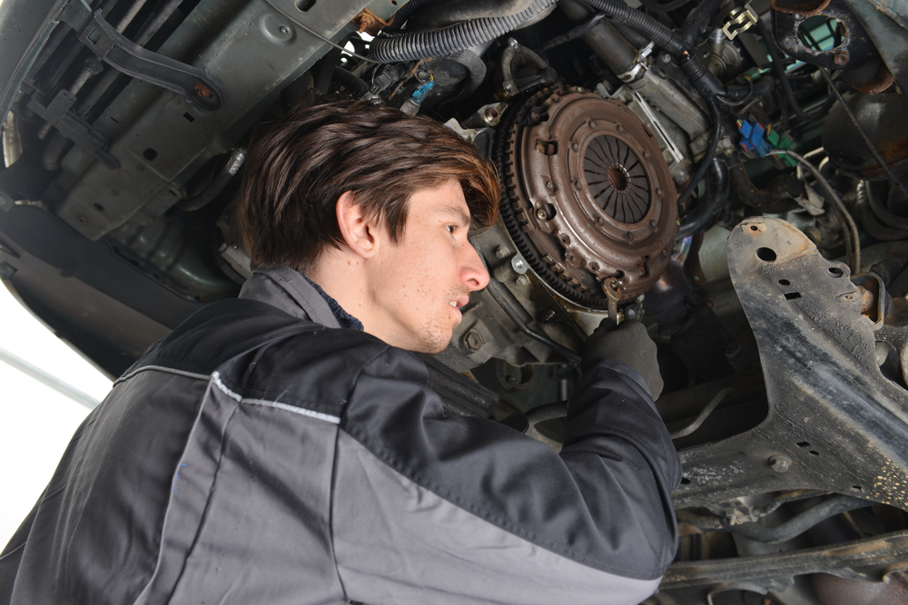 Auto mechanic working under the car and changing clutch at car repair shop