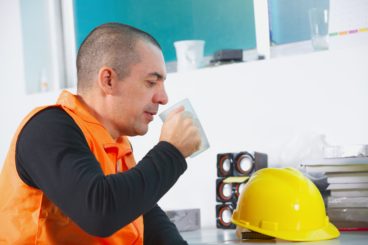 site worker with orange jacket on and yellow hard hard sipping a cup of tea while on a break