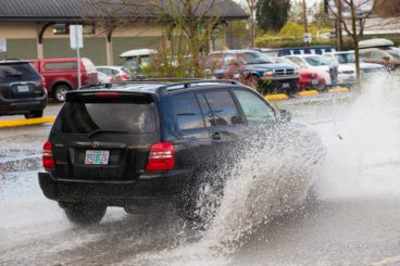 dark coloured car driving through big muddy puddle on the street