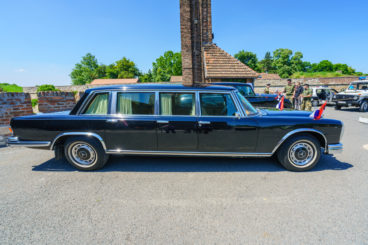 Black Mercedes-Benz 600 Pullman with a country house and trees in the background in colour