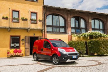 a bright red fiat fiorino parked in front of yellow house on pebble road