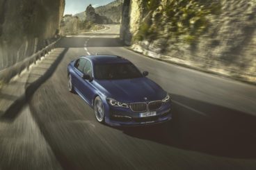 blue metallic bmw alpina driving fast down road with blurred cliffs in the background