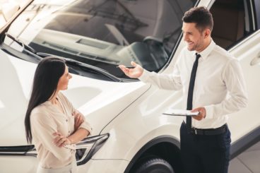 Beautiful young woman is talking to handsome car dealership worker while choosing a new car in dealership