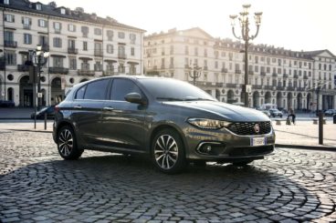a dark coloured fiat tipo parked on cobble road in European city in the background