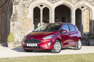 maroon coloured ford fiesta parked infront of vintage building with grass in front of it