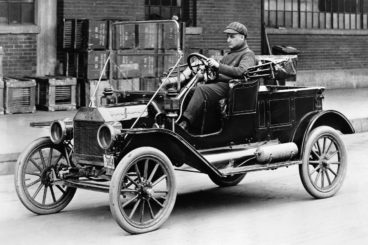 Black and white photo of a man driving a black Ford Model T
