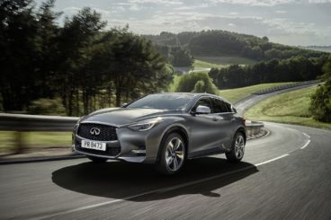 metallic grey infiniti Q30 hatchback driving up tarmac road with green trees and grass in the background