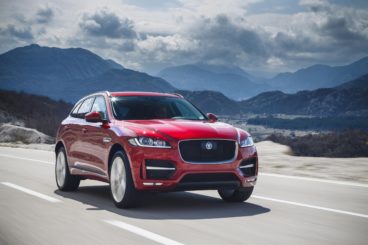 bright red jaguar f pace diesel driving on tarmac road with mountains in the background