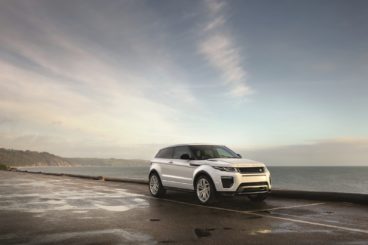 a white range rover evoque parked on pavement in front of the sea