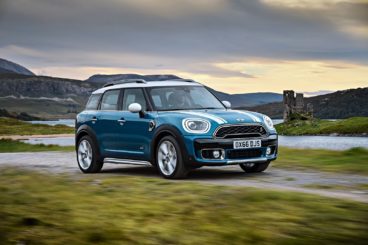 metallic blue mini countryman hatchback driving down country lane at sunset with blurred background