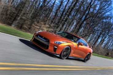 metallic orange nissan gt-r coupe driving on tarmac road with bare trees at the side