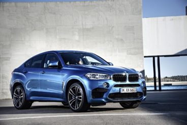 a metallic blue bmw x6 parked next to concrete building with ray of light shining on it