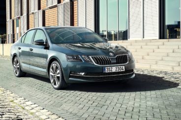 a metallic skoda octavia parked on a brick road next to a modern building