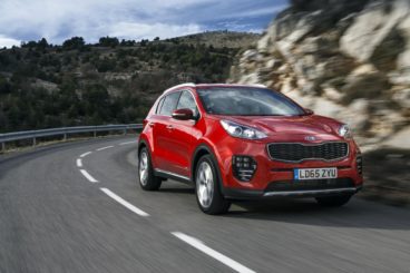 metallic red kia sportage driving on tarmac road with blurred cliffs in the background