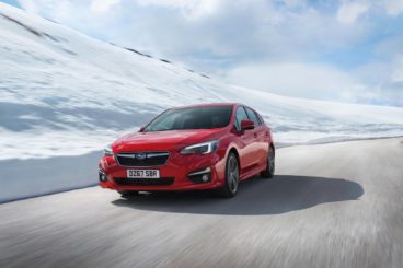 a metallic red subaru impreza hatchback driving on tarmac road with snow walls on either side