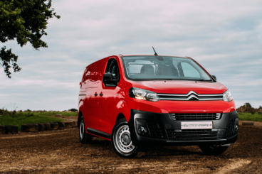 bright red citroen dispatch park on dirt road in the middle of green fields