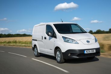 a white nissan e-nv200 combi estate driving on tarmac road with fields in the background