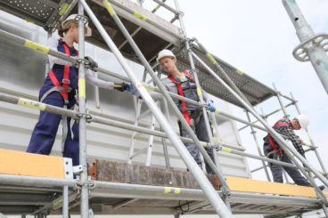 workmen on a construction site standing on scaffolding with hard hats and hi visibility jackets on