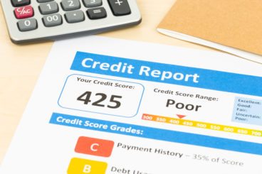 paper printout of a poor credit score of 425 with a calculator in the background