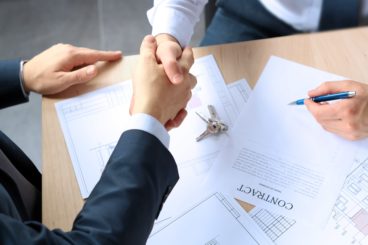 Men shaking hands agreeing on deal made over signed papers.