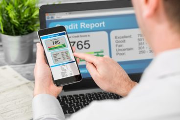 picture of a business man checking his phone and laptop that's showing a good credit score