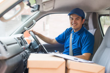 delivery man in a van with boxes on the passenger seat wearing a blue uniform and a blue cap