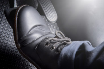 man with black shoes and blue jeans pushing down on the brake of a car