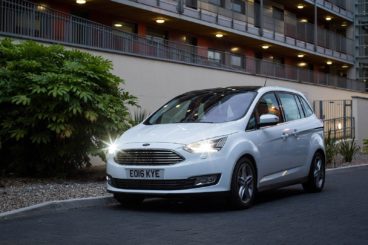 metallic white Ford Grand C MAX parked on tarmac road with modern building in the background