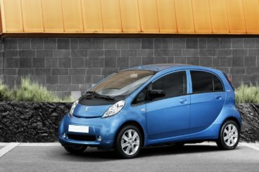 a metallic blue peugeot ion hatchback parked on tarmac infront of bright building