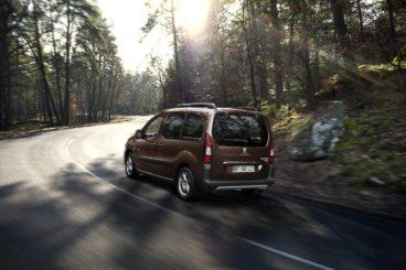 metallic peugeot partner tepee diesel estate driving on tarmac road in forest setting