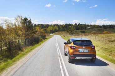 a metallic orange renault captur hatchback driving on tarmac road in a very green setting